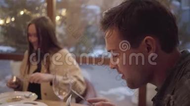两个朋友坐在靠近窗户的现代咖啡馆里吃饭。 红头发的年轻女子从深铝板上吃饭